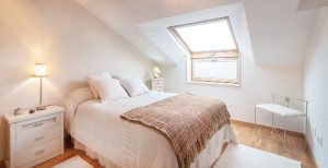 Habitación de cama matrimonial colores beige y blanco, con mesita de noche y lámpara de mesa.