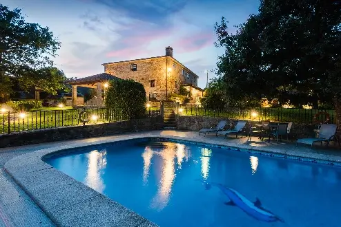 Foto de la piscina y la casa rural iluminada de noche.