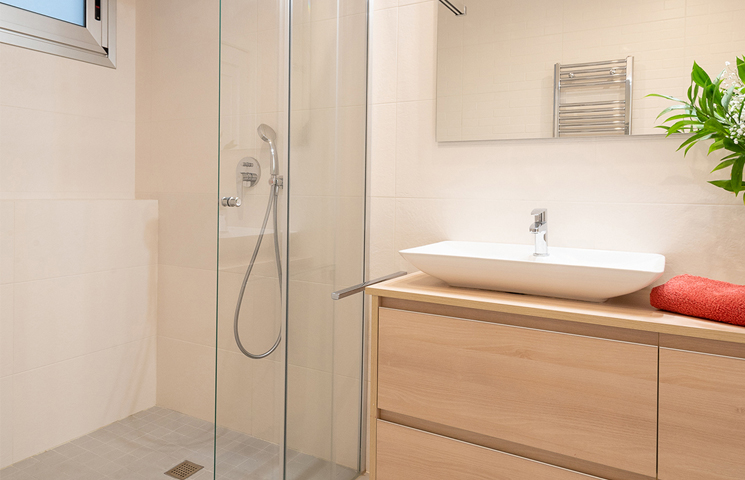 Fotografía de interiorismo y reformas de un baño con plato de ducha gris y mueble de lavabo color beige.